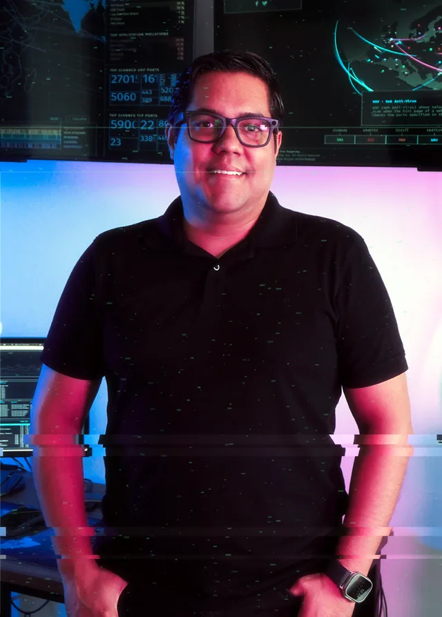 César Gaytán de pie en su estudio, con mapas de ciberseguridad al fondo